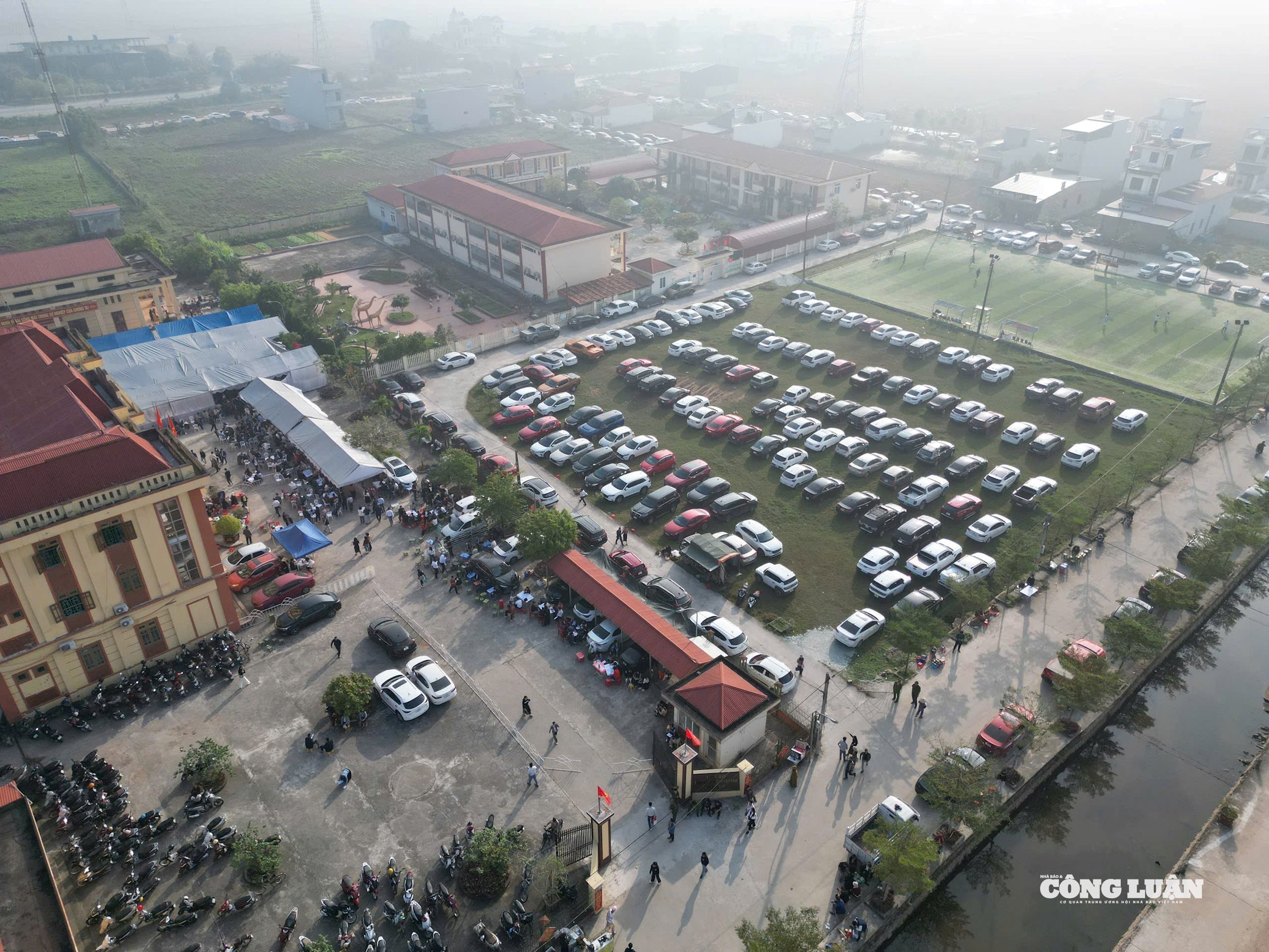 Nh&igrave;n từ tr&ecirc;n cao ph&iacute;a ngo&agrave;i s&acirc;n trụ sở Đảng ủy x&atilde; Kim Sơn được dựng nh&agrave; bạt, k&ecirc; ghế phục vụ phi&ecirc;n đấu gi&aacute; với &ocirc; t&ocirc; đỗ s&acirc;n v&agrave; c&aacute;c tuyến đường.